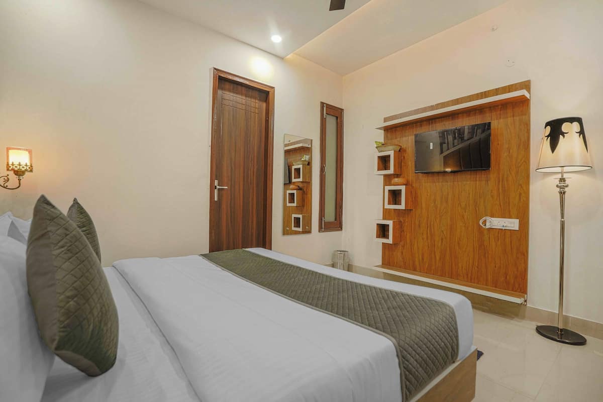 Een hotelkamer met een bed, een houten kledingkast, een aan de muur bevestigde televisie en een vloerlamp.