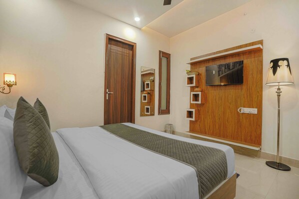 Una habitación de hotel con una cama, un armario de madera, un televisor montado en la pared y una lámpara de pie.