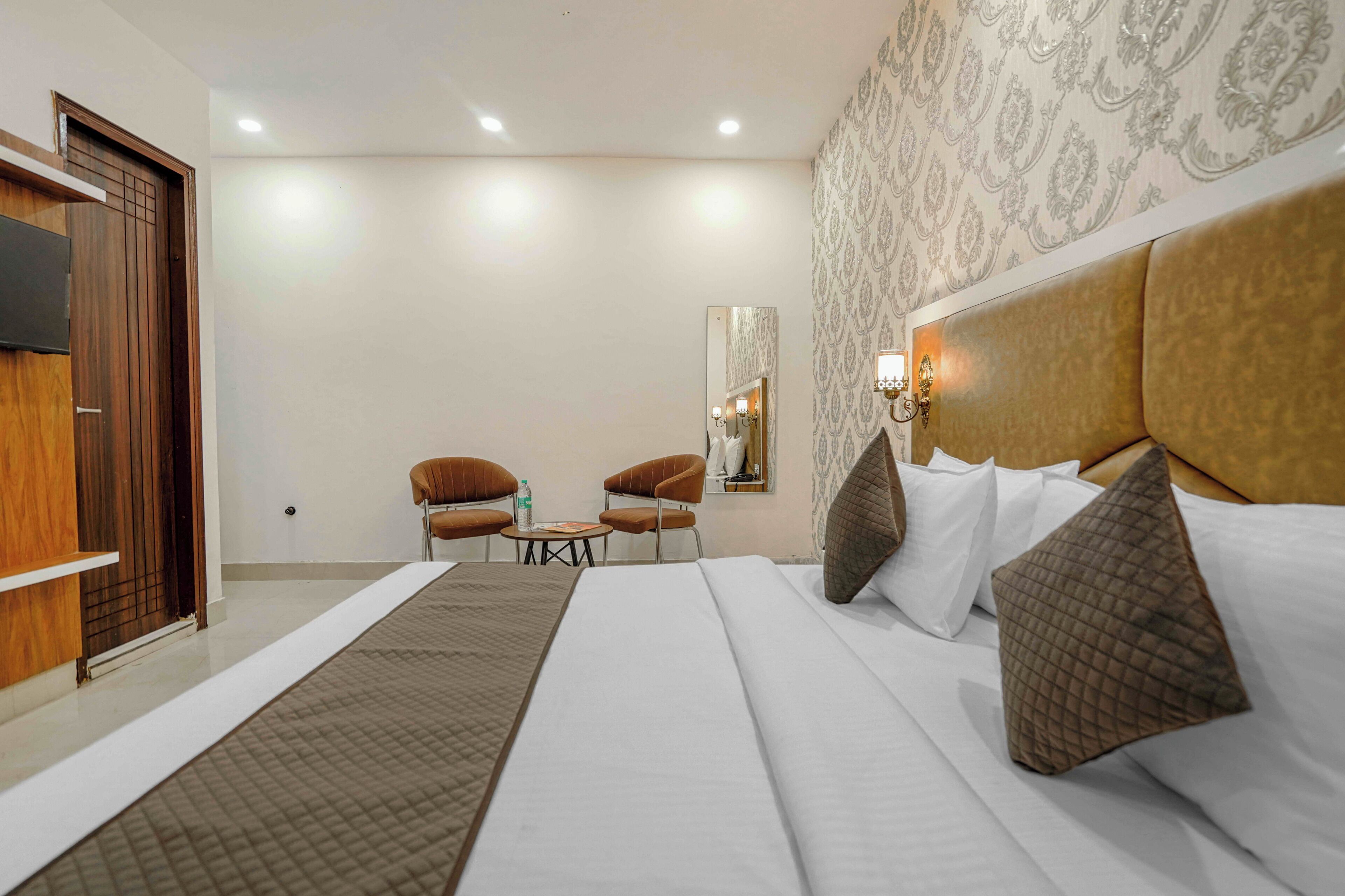 A hotel room with a large bed, two armchairs, a small table, and a mirror on the wall.