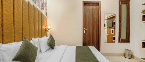 Camera d'albergo con un letto grande, una testiera, una porta in legno e un cestino dei rifiuti.
