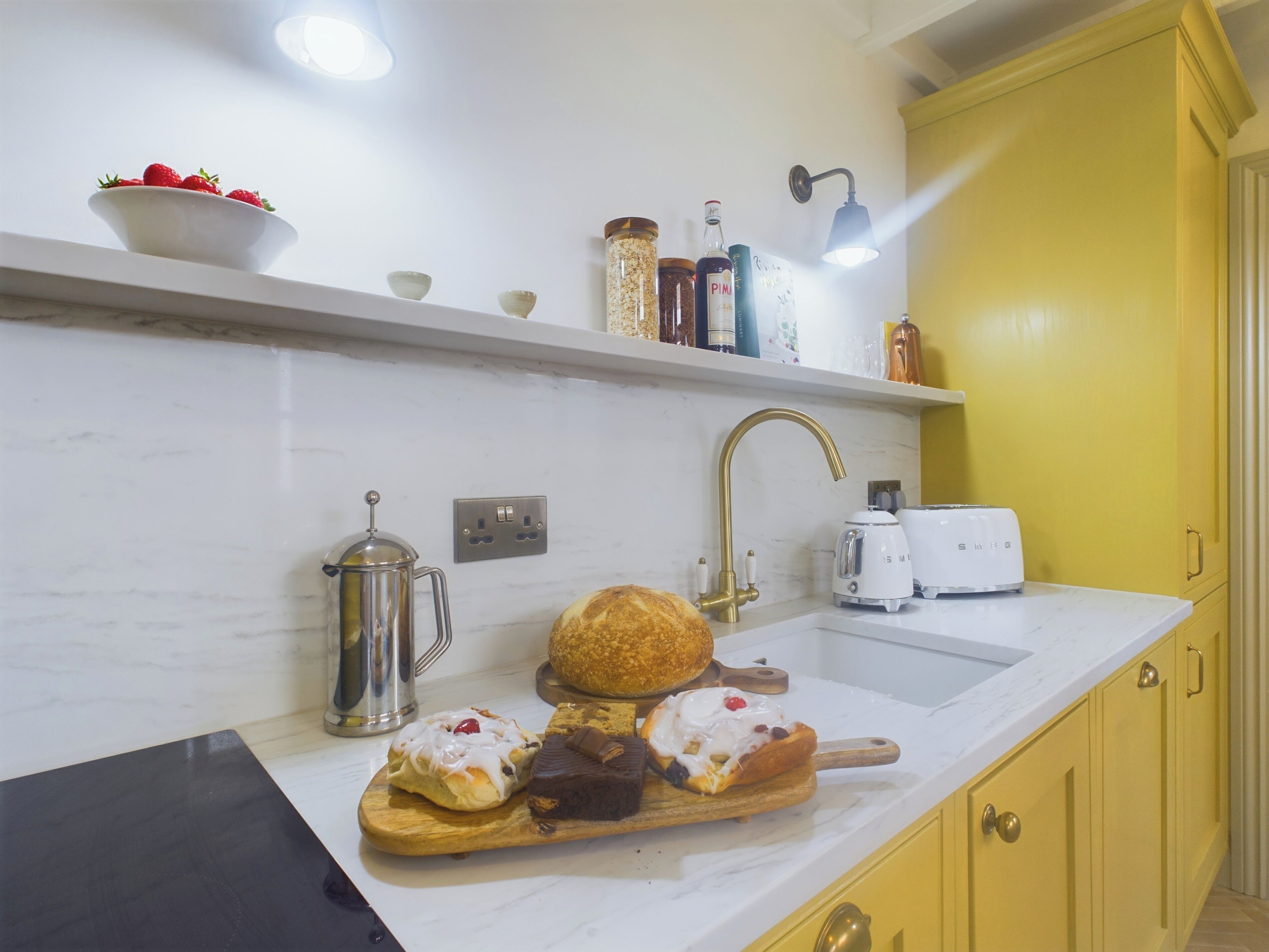 Cozinha com bancada de mármore, cafeteira de aço inoxidável, torradeira e tábua de corte de madeira com doces.