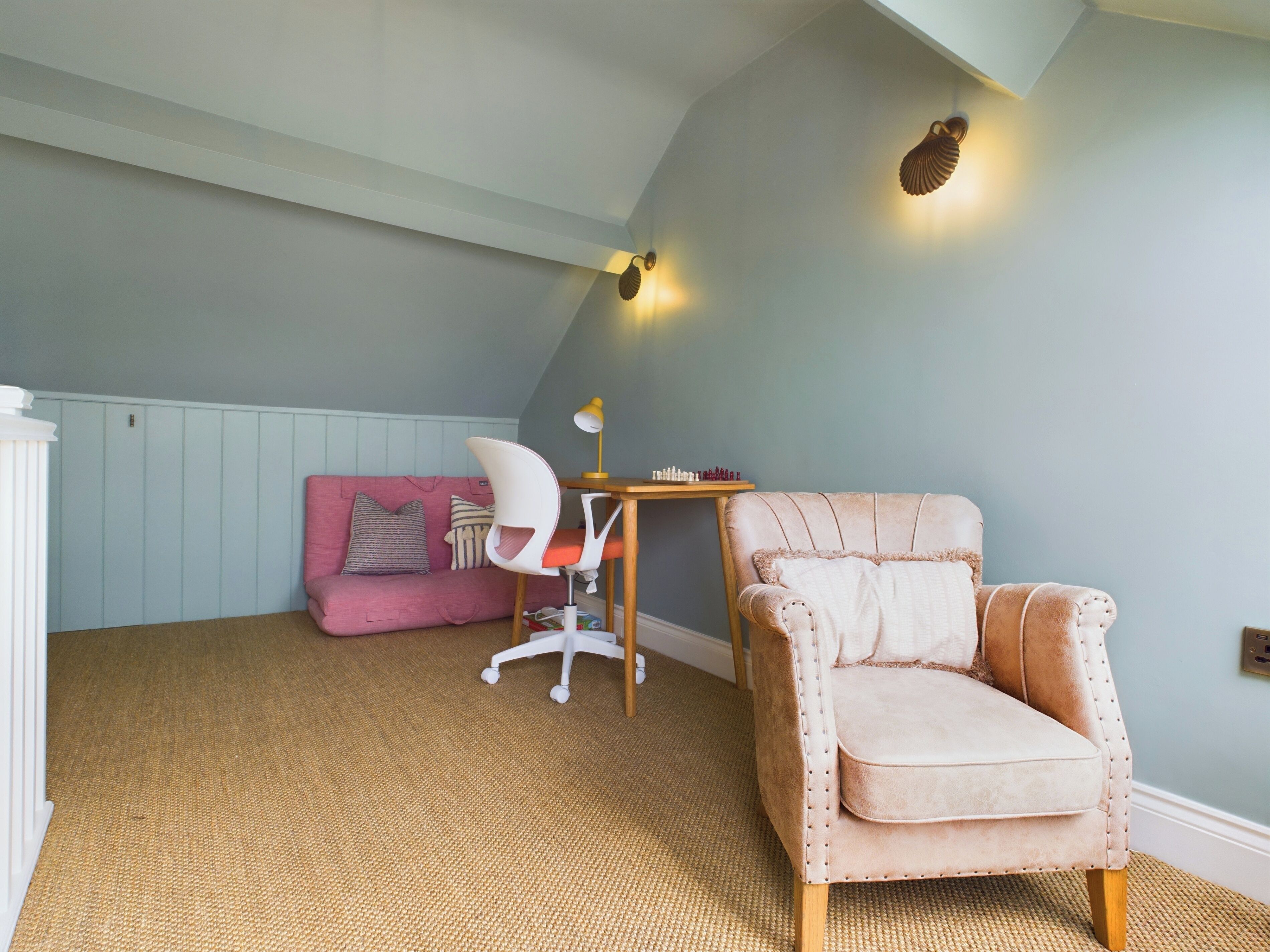 A cozy room with a pink sofa, a white chair, and a beige armchair. There is a small table with a lamp and a wall-mounted light fixture.