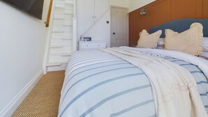 Un dormitorio con cama, televisor en la pared, una escalera y una puerta.