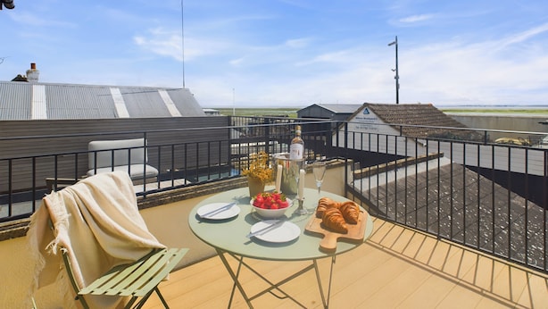 Una terraza en la azotea con una mesa lista para dos, que incluye una botella, un cuenco de fresas y un croissant.