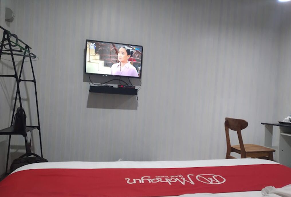 Een hotelkamer met een bed, een aan de muur bevestigde televisie, een houten stoel en een plank met een tas.