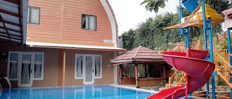 A swimming pool with a red slide, a gazebo, and a building with a curved roof.