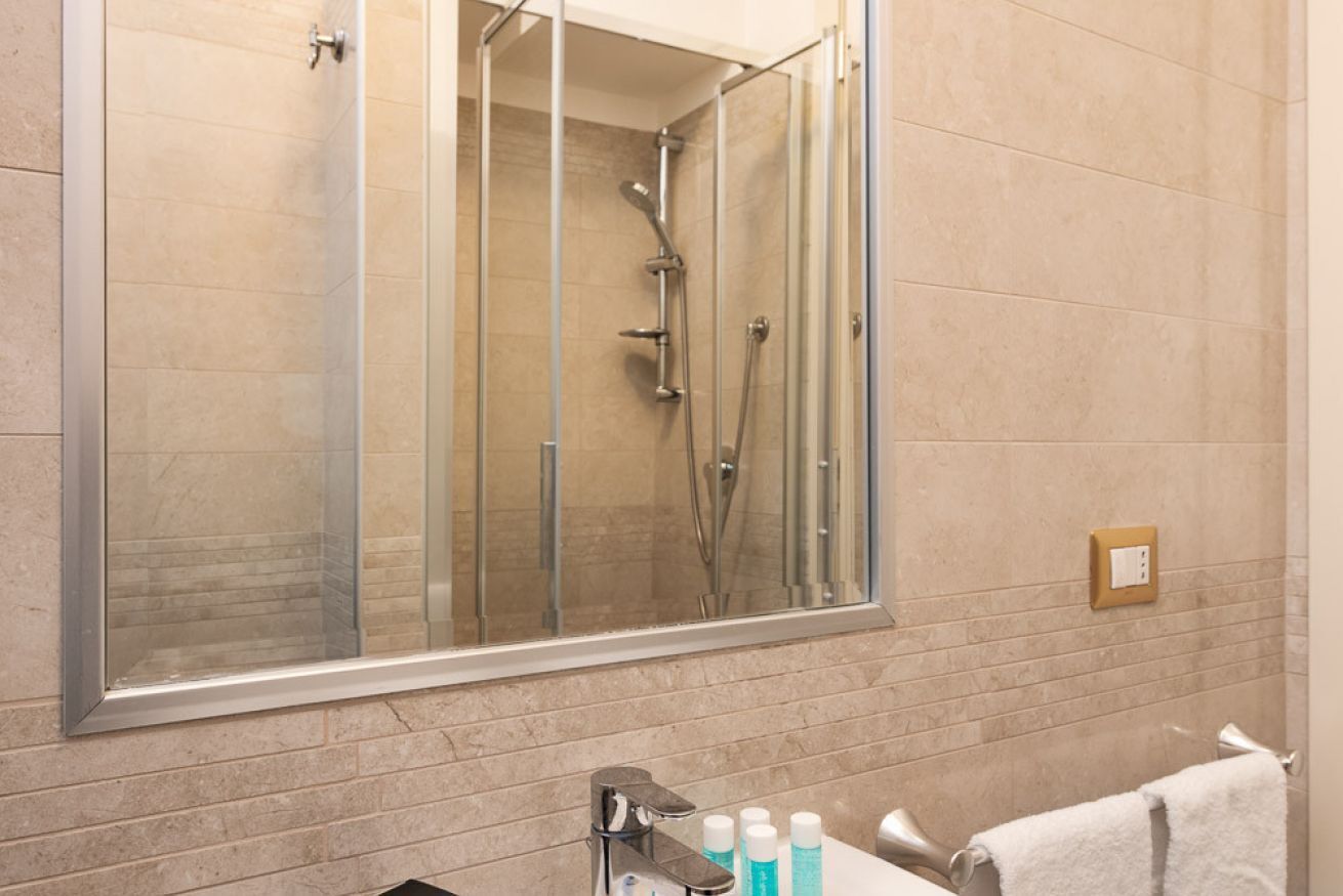 A modern bathroom with a glass-enclosed shower, a large mirror, and a sink with toiletries.