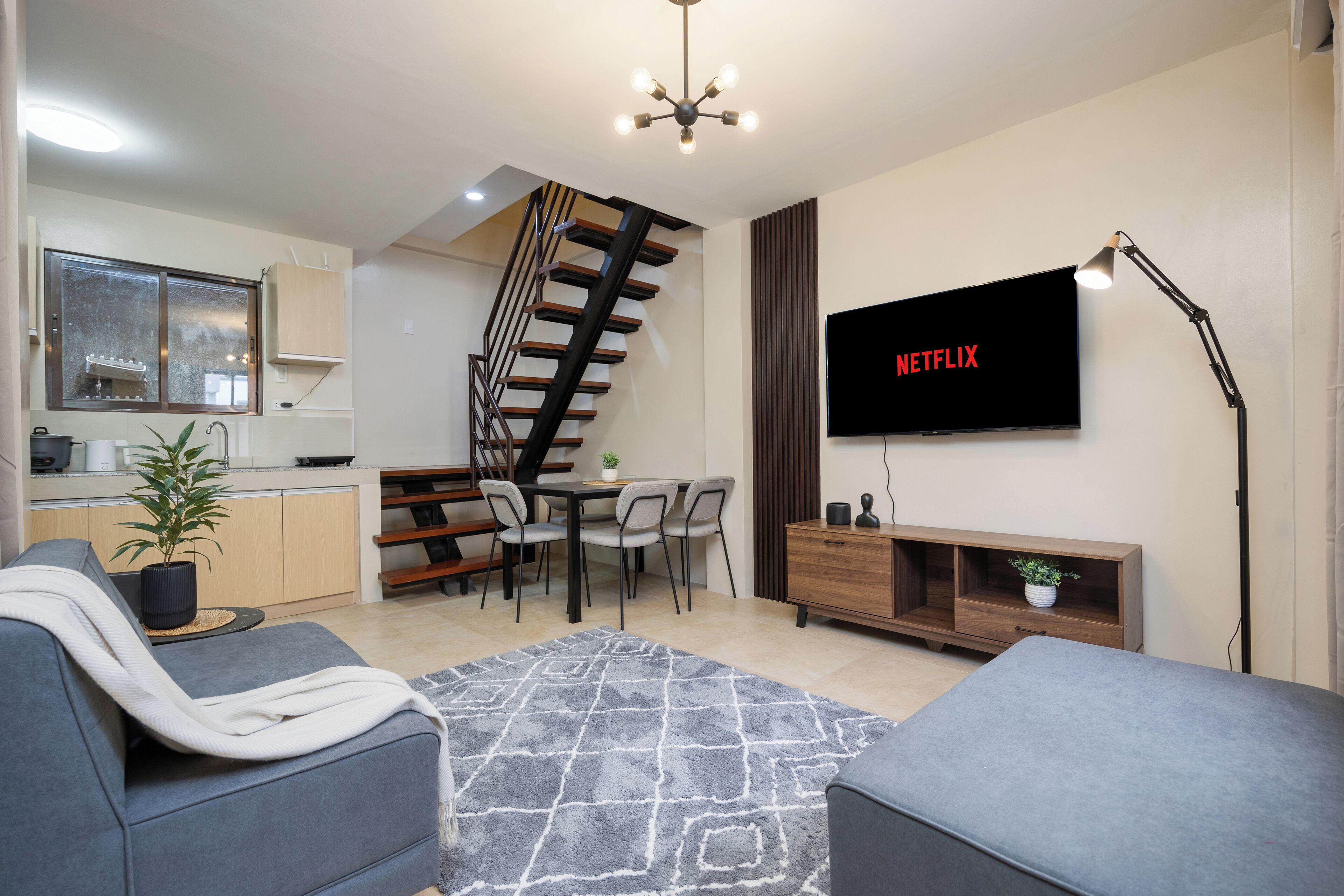 A modern living room with a staircase, a dining area, and a kitchen.