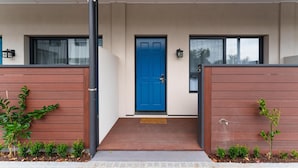 Une entrée moderne, avec une porte bleue, un petit seuil et une rampe métallique.