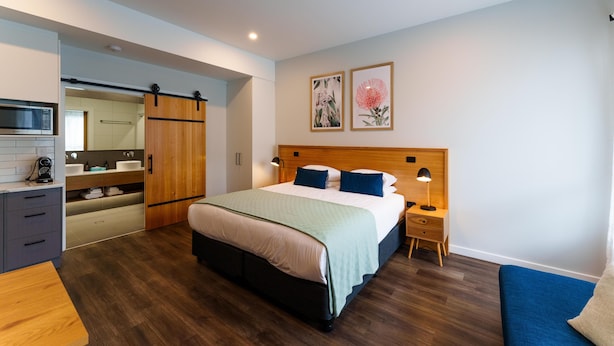 Une chambre à coucher moderne, avec un lit, des tables de chevet, une armoire, un miroir et des œuvres d’art accrochées au mur.
