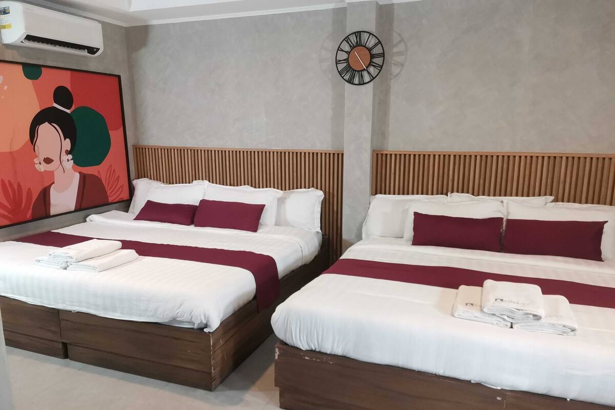A hotel room with two beds, a wall clock, and an air conditioning unit.