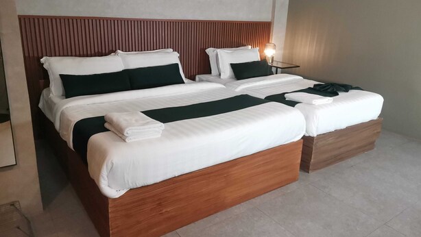 Una cama doble con cabecera de madera, ropa de cama blanca y un detalle en color verde.