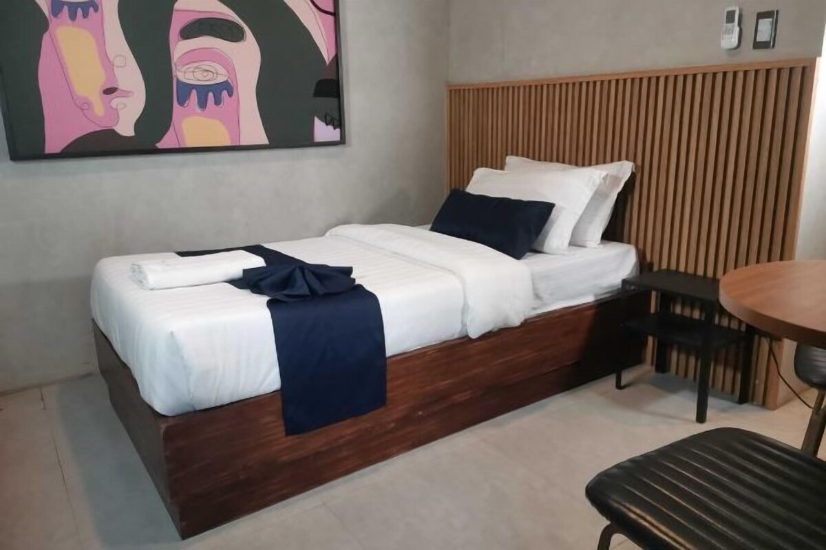 A single bed with a wooden headboard, a bedside table, a chair, and a painting on the wall.
