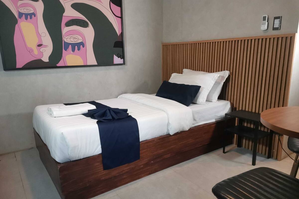 A single bed with a wooden headboard, a small round table, and a chair.