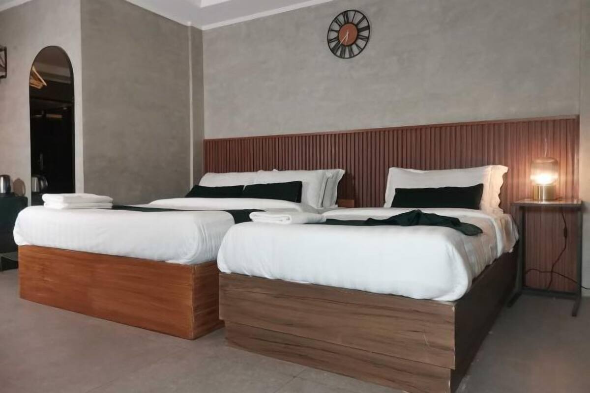A double bed with wooden headboard and white bedding, a bedside table with a lamp, and a clock on the wall.