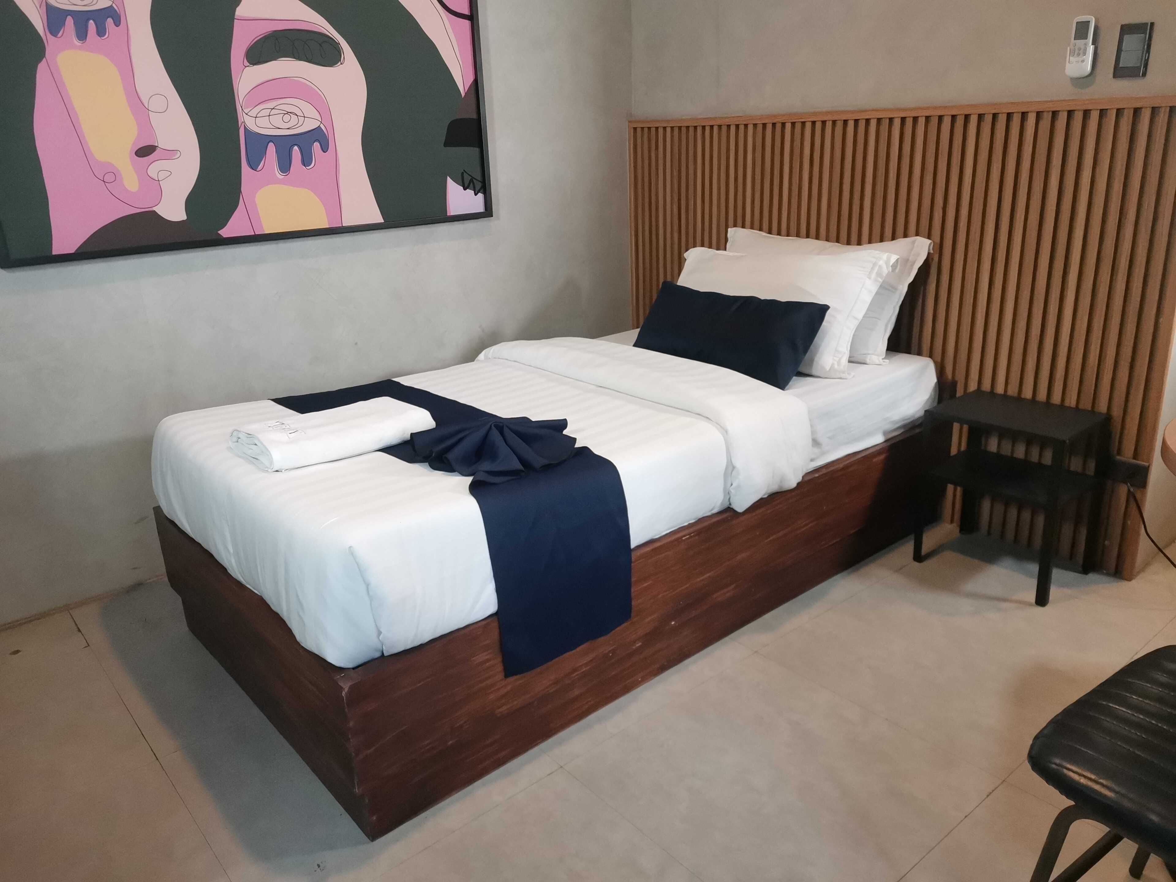 A single bed with white bedding and a dark blue throw, a wooden headboard, a small bedside table, and a wall-mounted phone.