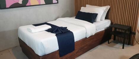 A single bed with white bedding and a dark blue throw, a wooden headboard, a small bedside table, and a wall-mounted phone.