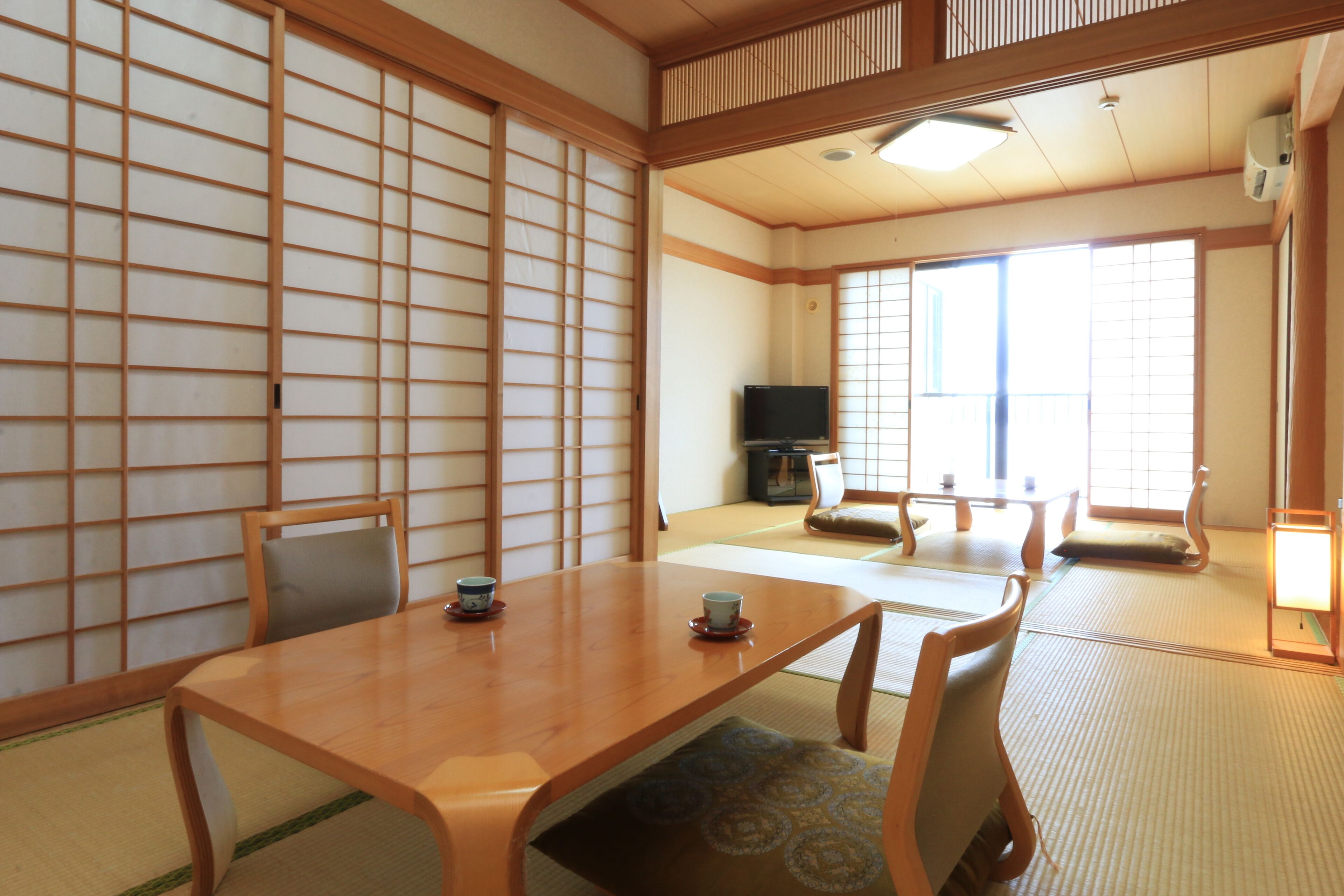 Une pièce de style japonais traditionnel, avec un sol recouvert de tatamis, une basse table en bois entourée de coussins et des portes coulissantes.