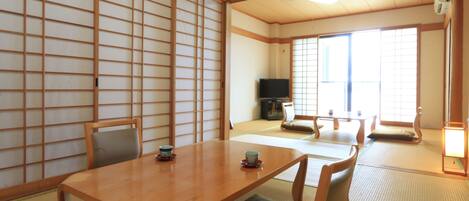 Une pièce de style japonais traditionnel, avec un sol recouvert de tatamis, une basse table en bois entourée de coussins et des portes coulissantes.