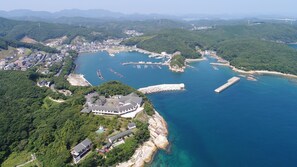An aerial view of a coastal area with a marina, residential buildings, and a large building with a sloped roof. - Tsushima Grand Hotel (Tsushima)