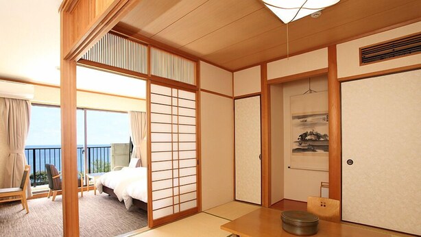 Een traditionele Japanse hotelkamer met tatami vloeren, een bed, een tafel met een theeset en een schuifdeur naar een balkon.