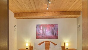 Un lit en bois avec deux tables de chevet, chacune équipée d’une lampe, dans une pièce dotée d’un plafond en bois et d’une décoration murale sur le thème de la forêt.