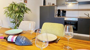 Une cuisine moderne équipée d’une cuisinière, d’un four et d’une machine à café. On y trouve une table à manger avec des assiettes, des verres et une bouteille de vin.