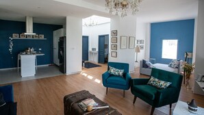 A spacious living area with a modern kitchen, a chandelier, and a blue accent wall. - La Villa Des Oliviers (Site archéologique de Carthage)