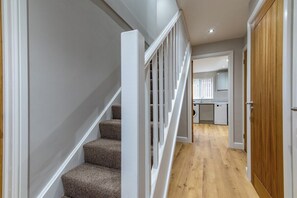 A hallway with a staircase, wooden flooring, and a kitchen area with cabinets and appliances.