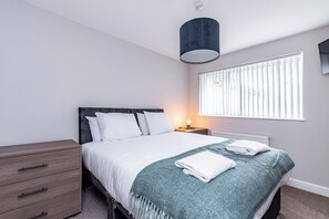 A bedroom with a bed, bedside table, lamp, and a window with blinds.