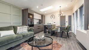 A modern living room with a sofa, coffee table, and a dining area with a bench and chair. - Lodge No 25 | St Andrews Lodge Park (Strathkinness)