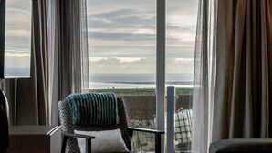 A room with a view of the sea through a large window, a chair with a blanket, and a television on the wall. - Lodge No 25 | St Andrews Lodge Park (Strathkinness)