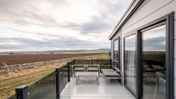 A modern balcony with a view of a rural landscape, featuring a glass door and a metal railing. - Lodge No 25 | St Andrews Lodge Park (Strathkinness)