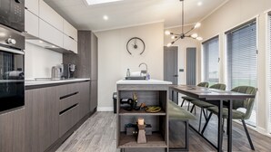 A modern kitchen with built-in appliances, a dining area with a table and chairs, and a clock on the wall. - Lodge No 25 | St Andrews Lodge Park (Strathkinness)