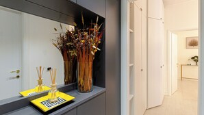 Un baño moderno con un espejo, un lavamanos con una bandeja amarilla y un jarrón con flores secas.
