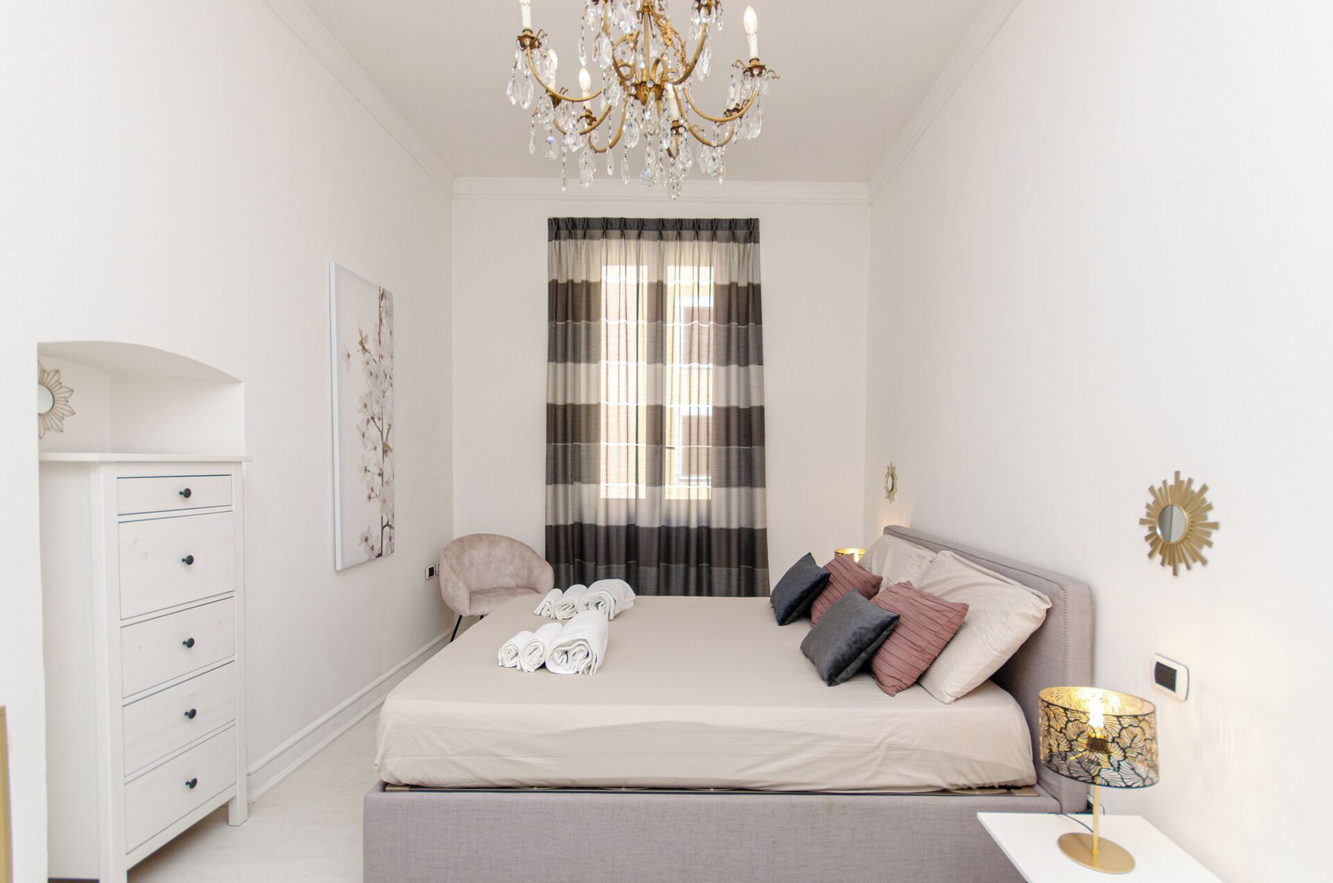 A bedroom with a bed, bedside table, lamp, and a dresser.