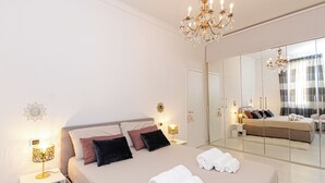 Un dormitorio moderno con una cama grande, lámparas de noche, una araña y un espejo de cuerpo entero que refleja la habitación.