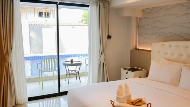 Habitación de hotel con una cama grande, una mesita pequeña, una silla y vista a una piscina a través de un ventanal corredero.
