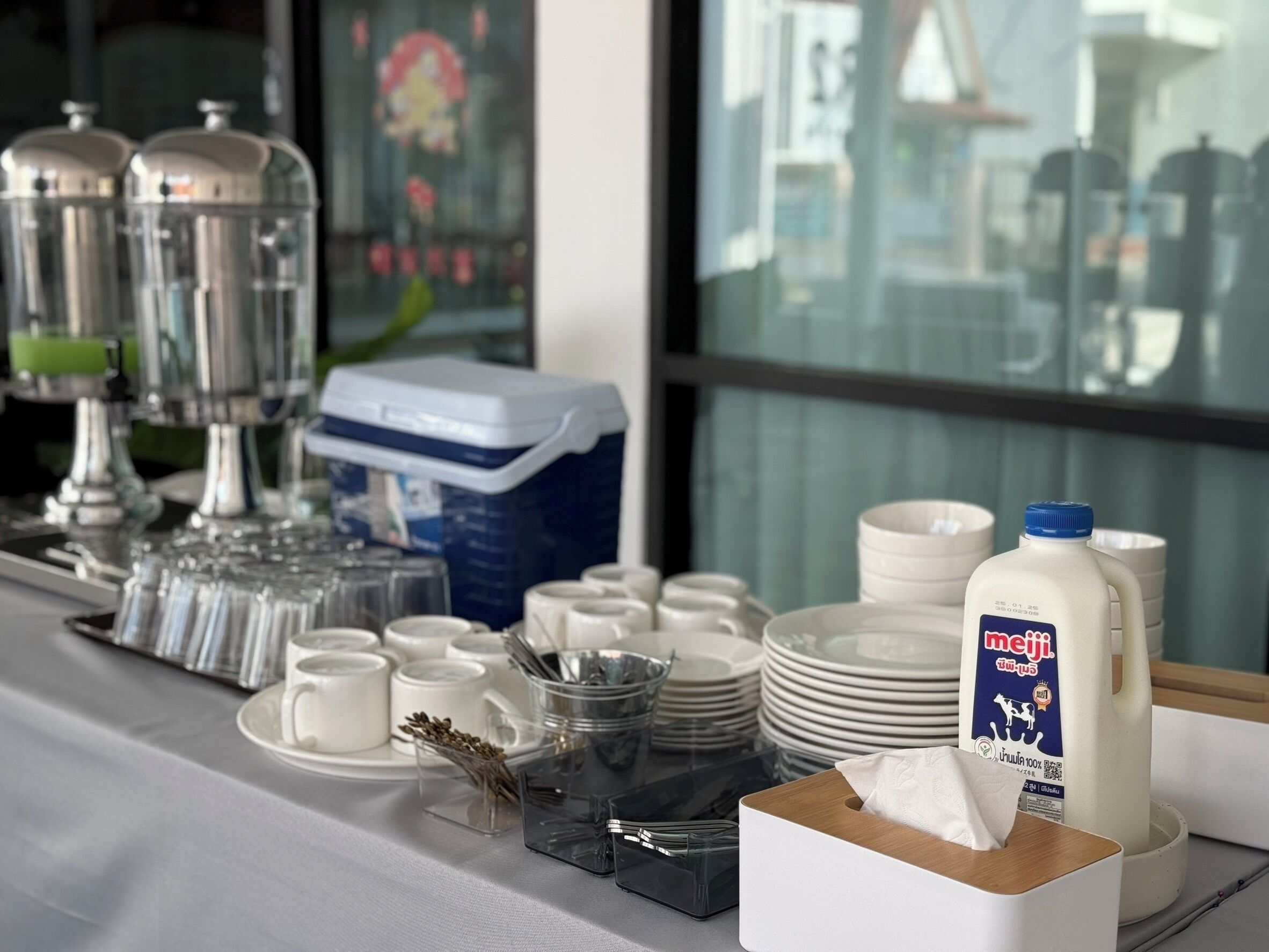 A buffet setup with clear glassware, plates, and a milk jug labeled "meiji".