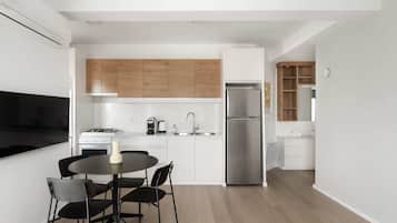 Eine moderne Küche mit weißen Schränken, einem Edelstahlkühlschrank, einem Esstisch mit Stühlen und Holzboden.