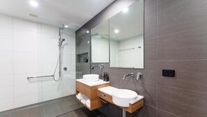Un baño moderno con cabina de ducha de vidrio, dos lavamanos, un espejo y un mueble de tocador de madera.