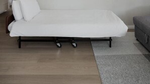 A minimalist room with a single bed, a small sofa, and a wall-mounted light fixture. - Chic 8 Keren Hayesod (Jerusalem)