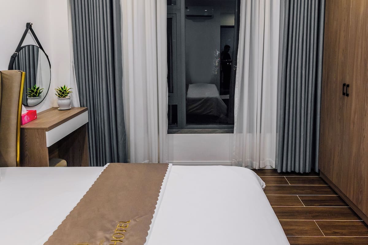 A hotel room with a bed, a desk with a mirror, a small plant, and a wardrobe.