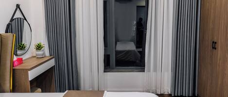 A hotel room with a bed, a desk with a mirror, a small plant, and a wardrobe.