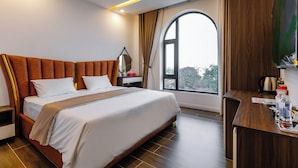 A modern hotel room with a large bed, wooden headboard, a desk with a chair, a large window, and a view of the city. - Times Hotel (Trảng Bàng)