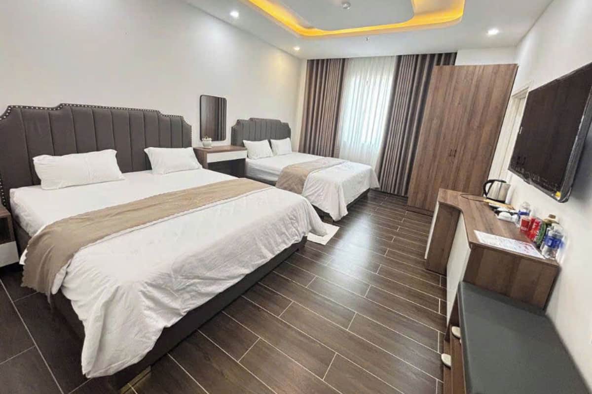 A hotel room with two beds, a desk, a TV, and a mirror.