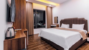A modern hotel room with a large bed, a wooden desk, a flat-screen TV, and a view of the city at night. - Times Hotel (Trảng Bàng)
