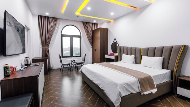A modern hotel room with a large bed, a desk, a chair, and a window with curtains. - Times Hotel (Trảng Bàng)