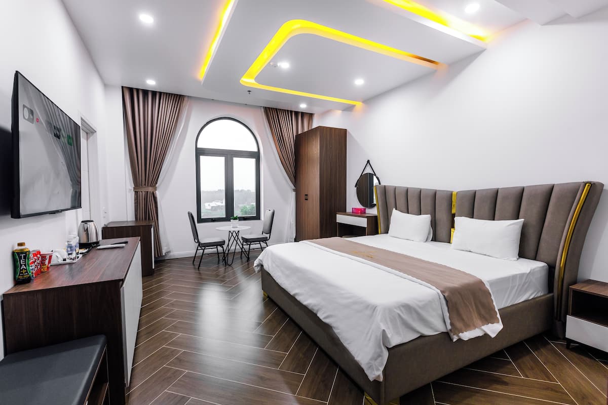 A modern hotel room with a large bed, a desk, a chair, and a window with curtains.