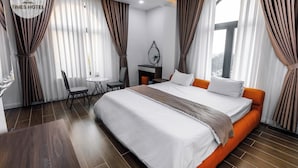 A hotel room with a large bed, a desk, a chair, and a view of the city. - Times Hotel (Trảng Bàng)